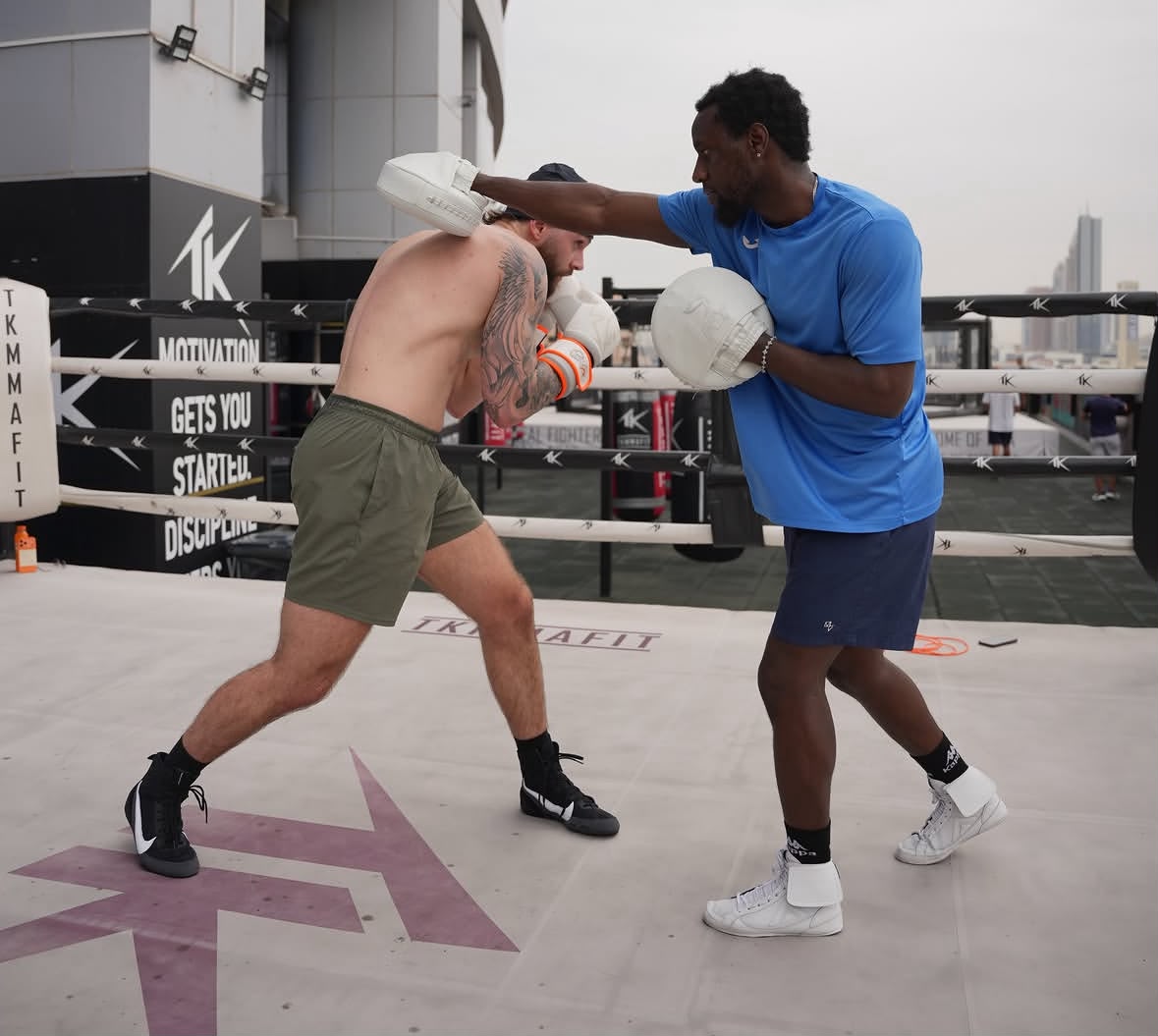 Coach Allid holding pads for a boxer in an outdoor ring
